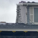 Residential roof installation in progress with ladders, tools, and roofing materials visible on the rooftop