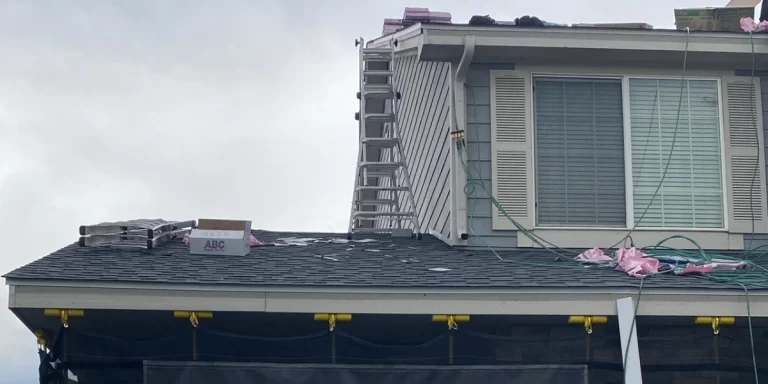 Residential roof installation in progress with ladders, tools, and roofing materials visible on the rooftop