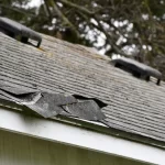 Torn and lifted asphalt roof shingles showing storm damage that requires professional roof repair assessment
