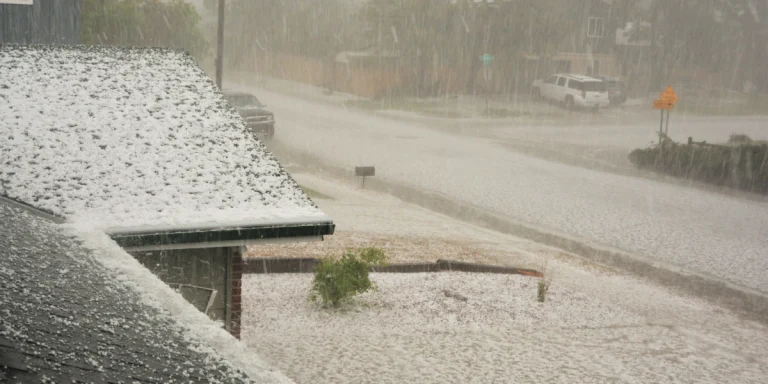 Intense hail storm covering a residential asphalt shingle roof and gutters with a thick layer of ice pellets.