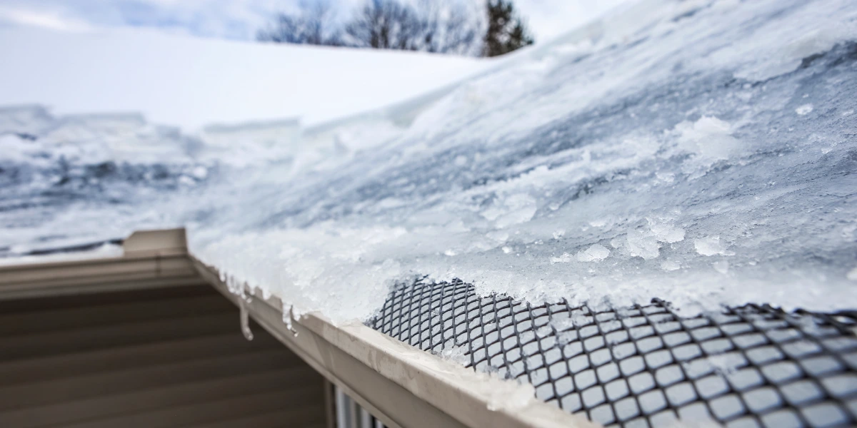 Snow and ice building up along a roof edge over a mesh gutter guard, with icicles hanging from the gutter.
